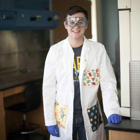 A young gentleman in a lab coat in a science classroom.