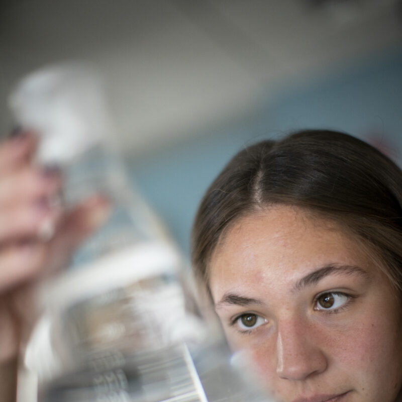 A young women measuring the amount of fluid in a science beaker.