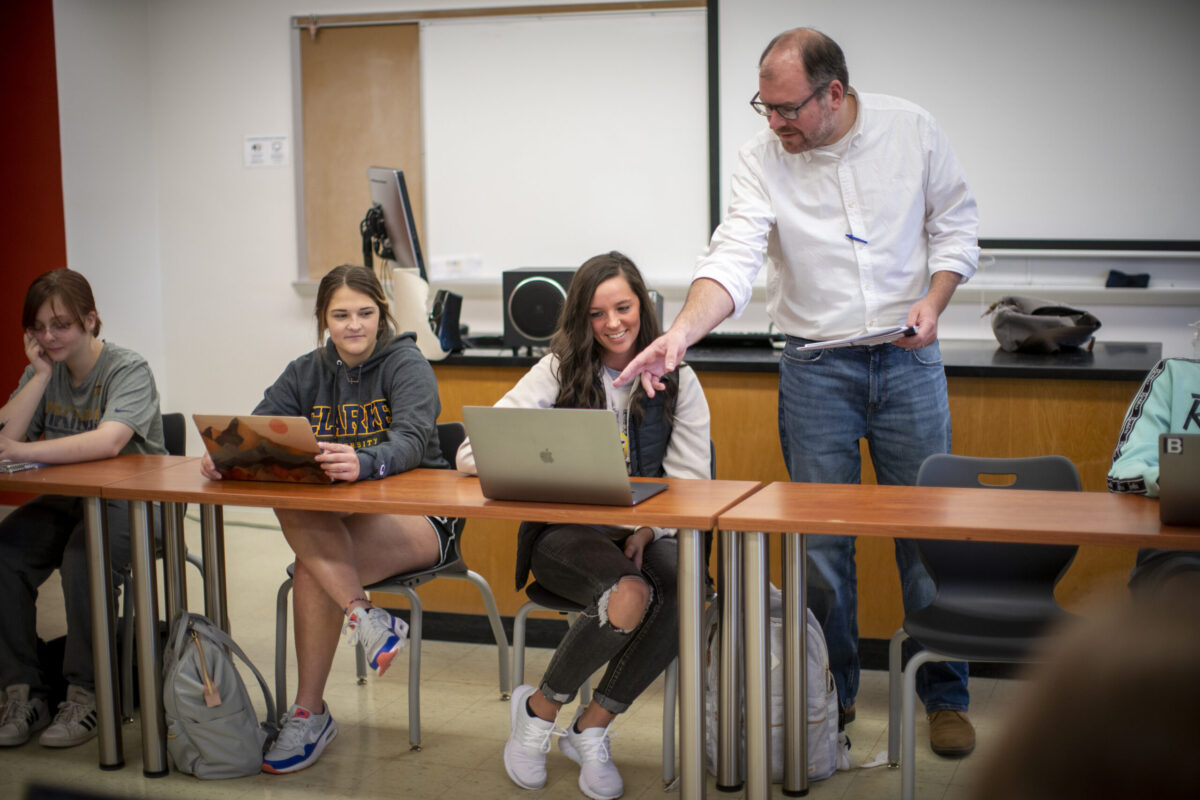 A male teacher standing over a student discussing the work on her laptop. - Full Size