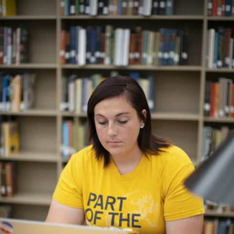 A female student in a library studying on her laptop.