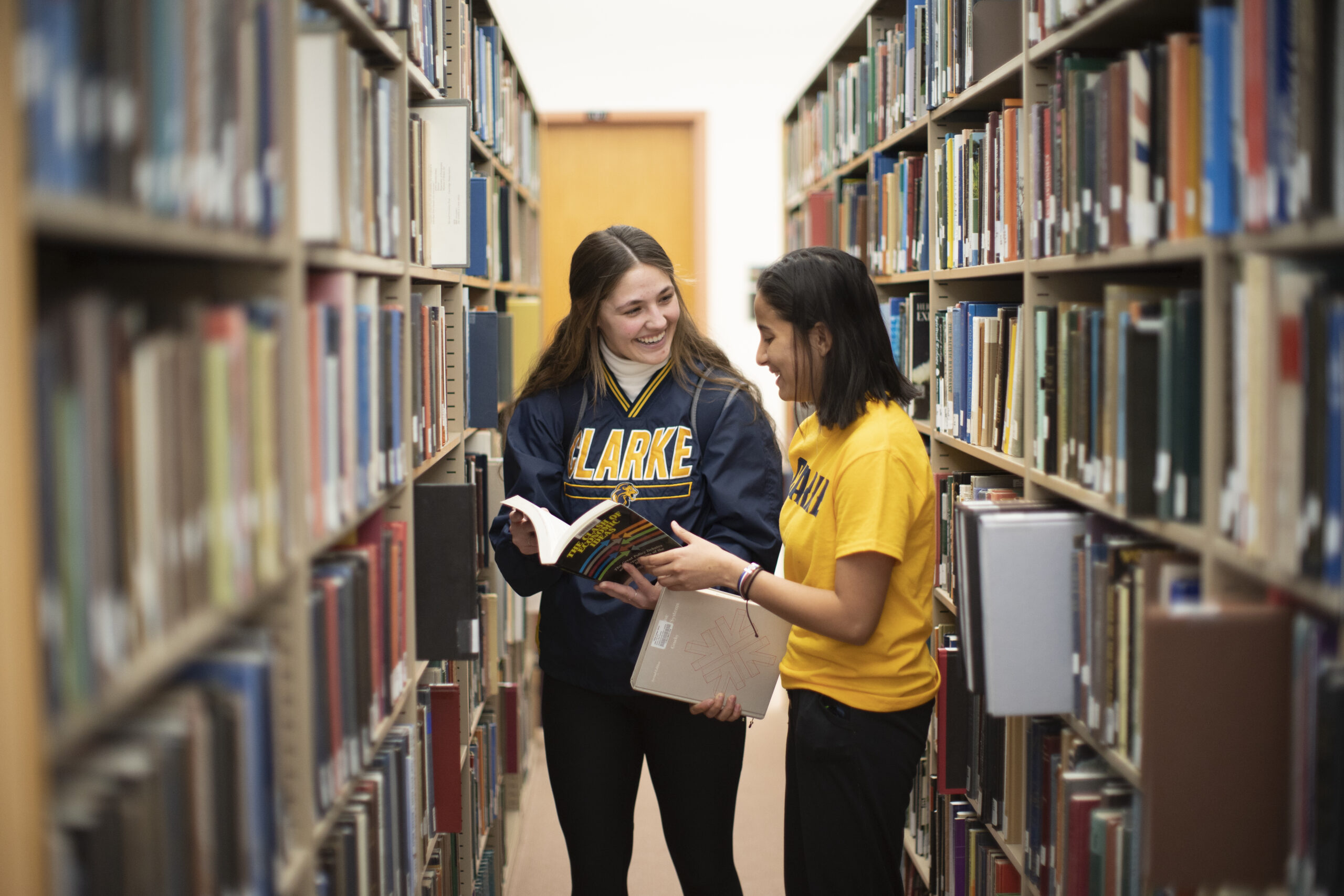 Two female students discussing the contents of a book in a library.